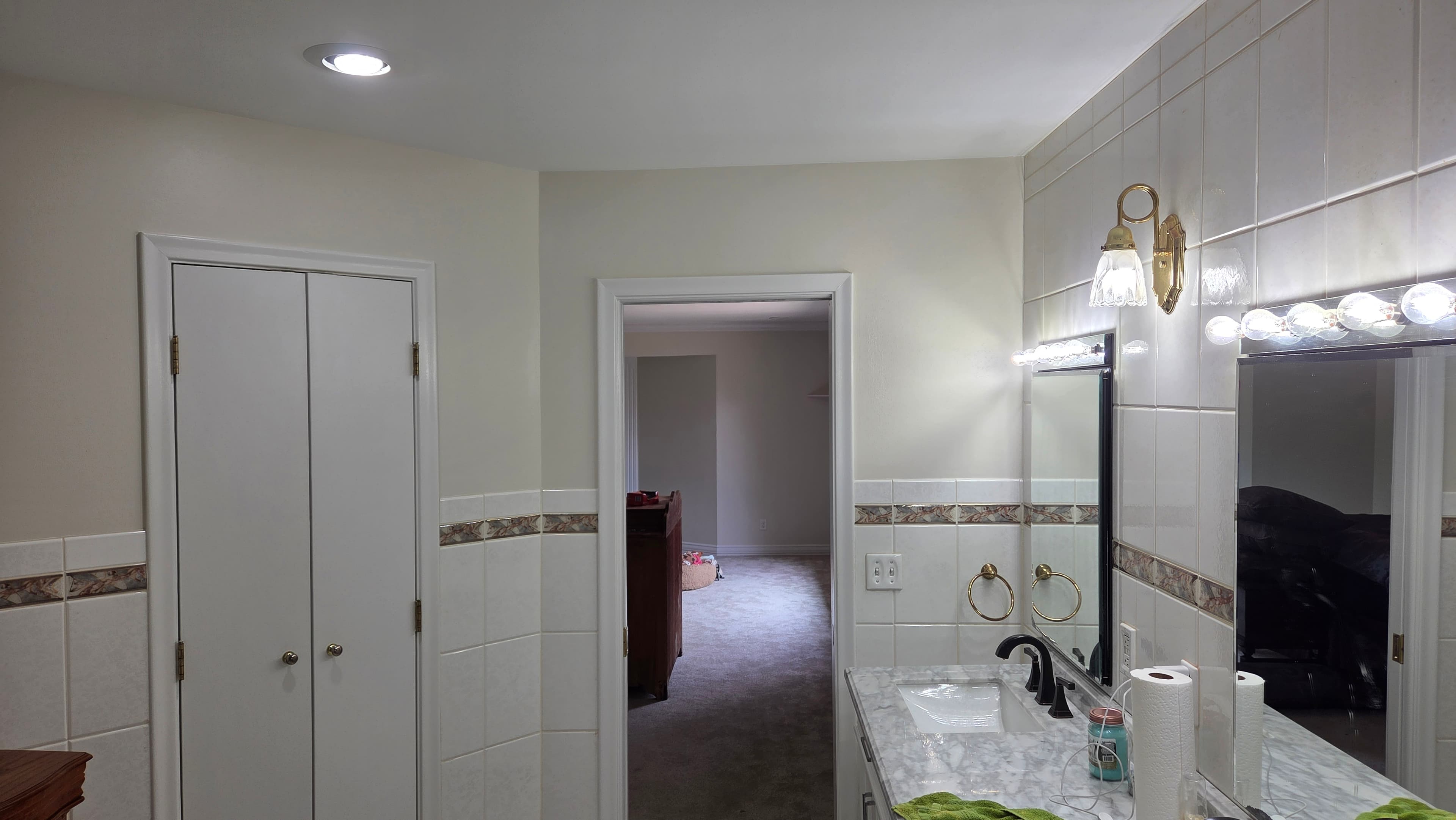 White tiled bathroom with marble vanity, black faucet, and doorway leading to a bedroom.