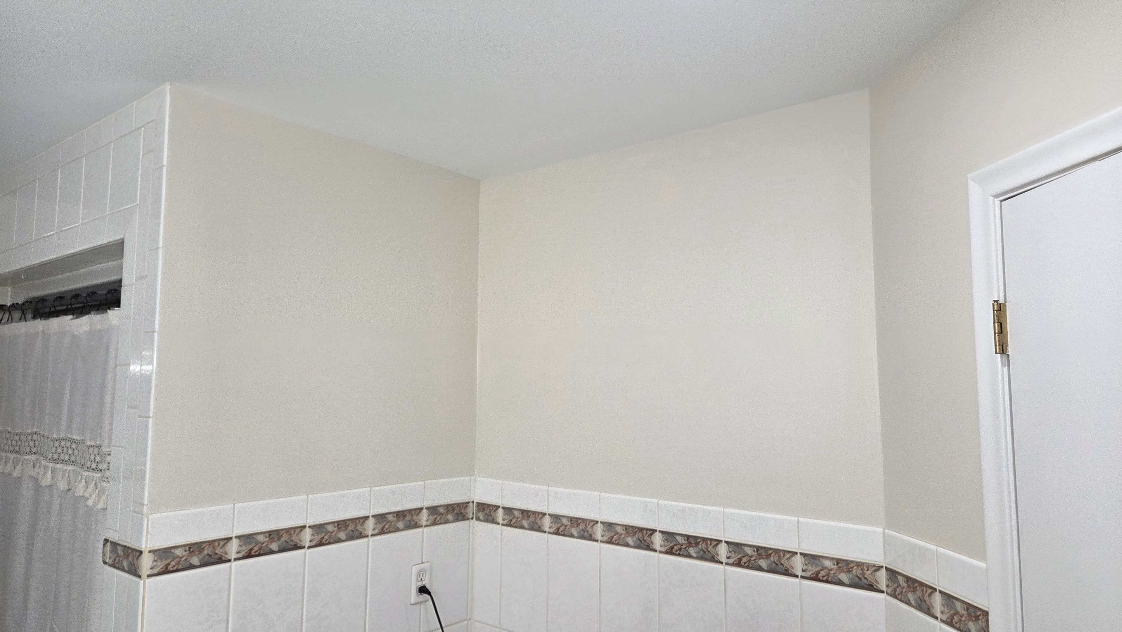Light beige bathroom corner with white wall tiles, a decorative border, and a white door.