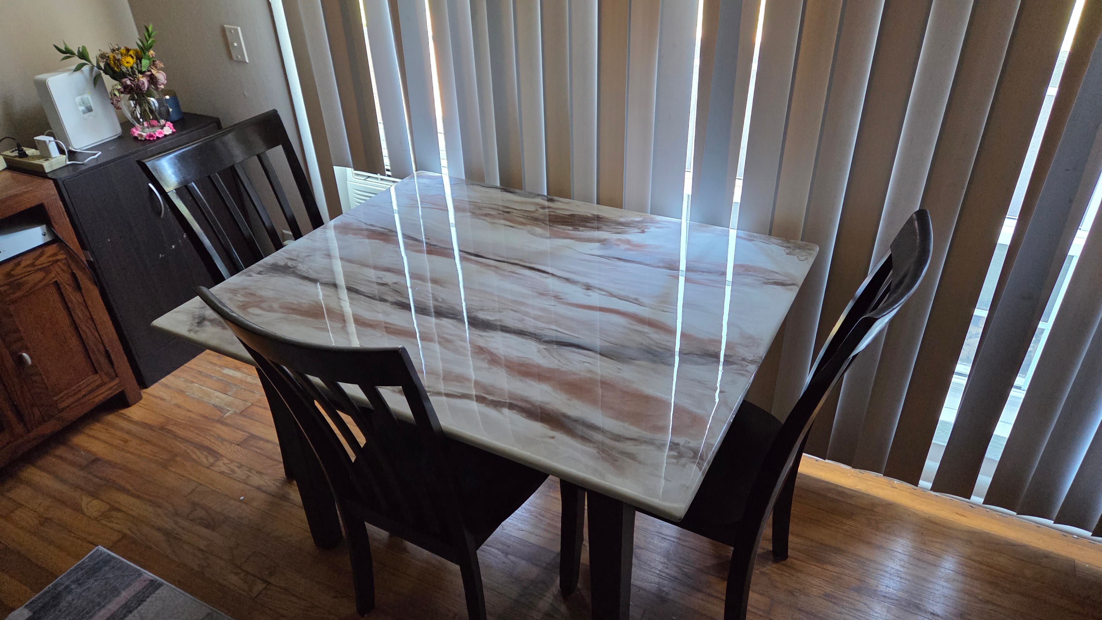 Glossy white and brown marbled epoxy dining table with dark wood chairs and vertical blinds.