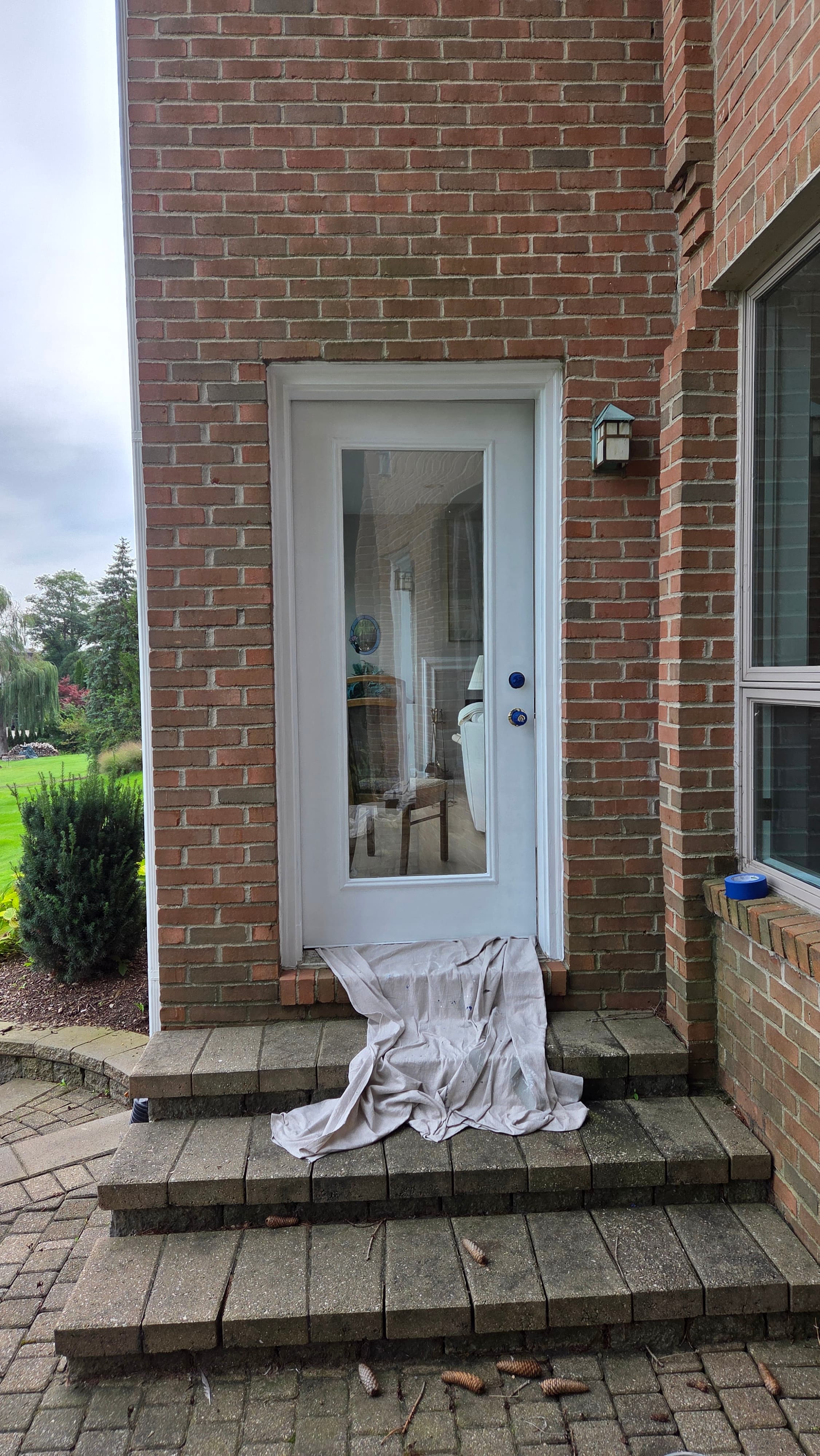 White glass door on a brick house with a drop cloth draped over stone steps.