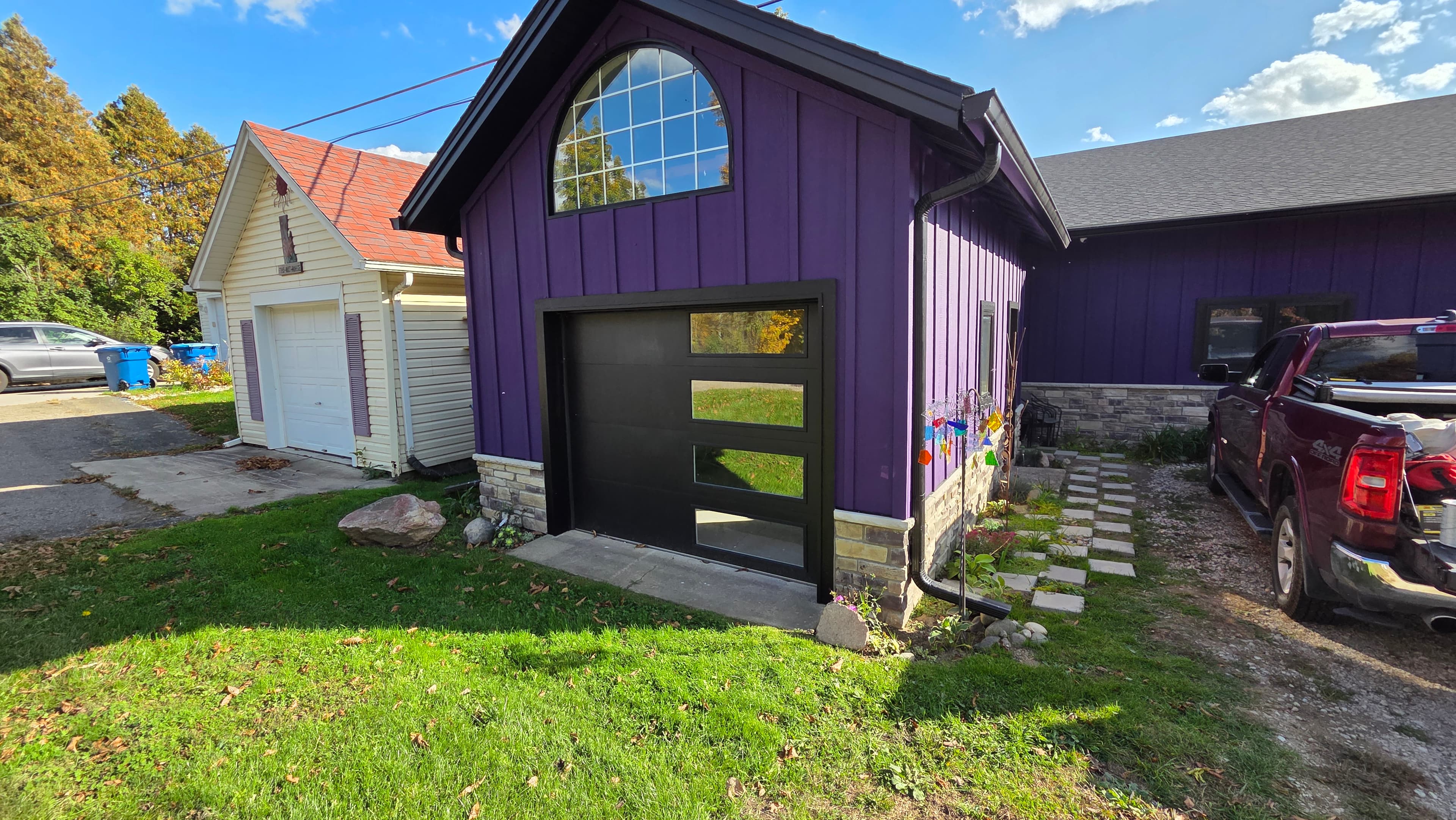 Vibrant purple garage with a black door and arched window next to a cream shed.